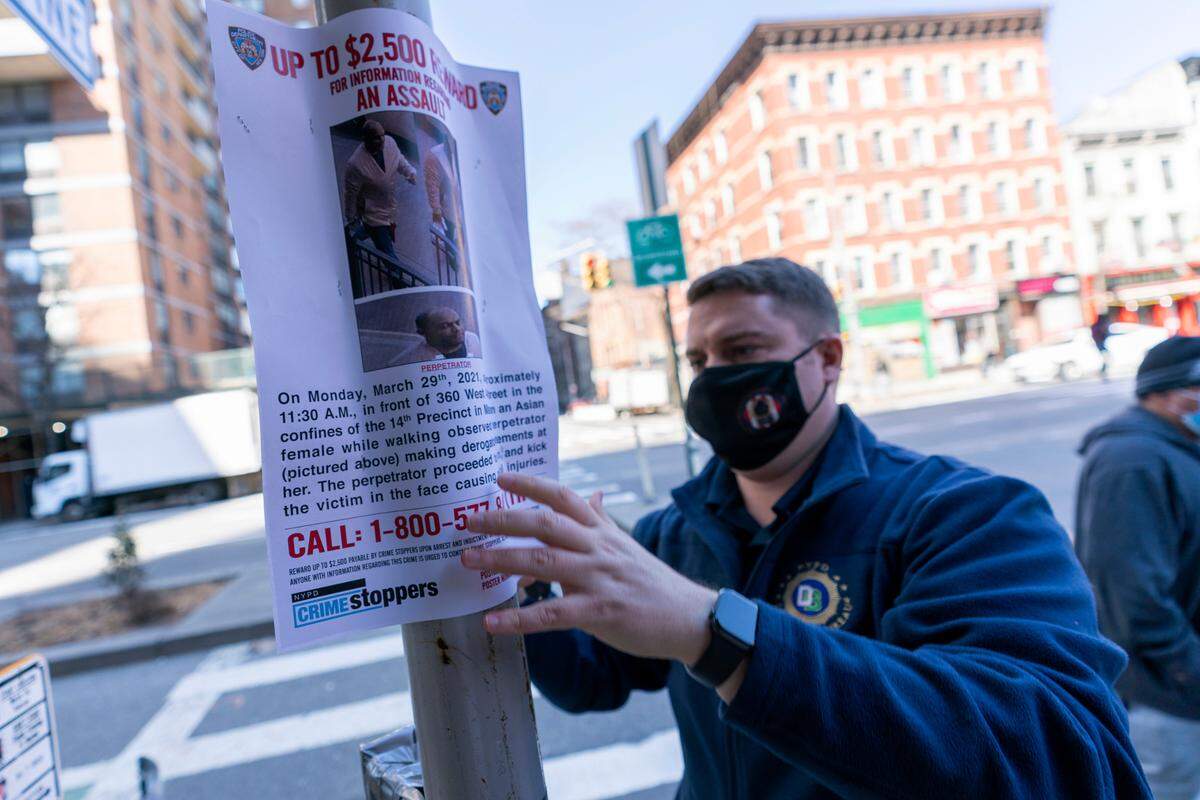 A police officer hangs a sign offering a reward for information on the person who attacked an Asian American woman near the crime scene, Tuesday, March 30, 2021, in New York. The New York City Police Department says an Asian American woman was attacked by a man Monday afternoon who repeatedly kicked her in front of witnesses who seemingly stood by. (AP Photo/Mary Altaffer)