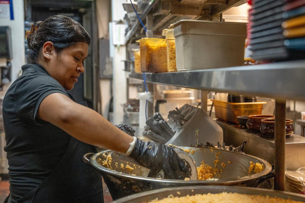 Food prepper Aracely Barragan scoops rice out of a large container to store away for the day’s service at Rudy’s Tenampa Taqueria.