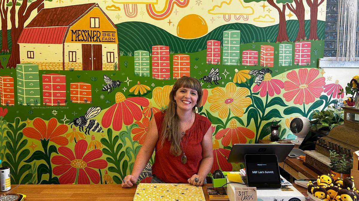 Owner Rachael Messner behind the counter at the new Messner Bee Farm shop in downtown Lee’s Summit. Artist Morgan Elliott painted the shop mural in the background.