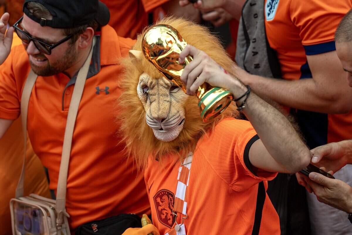 A fan wearing a lion mask holds a replica FIFA World Cup trophy while celebrating during the Orange Walk on Thursday, June 25, 2026, in Kansas City.