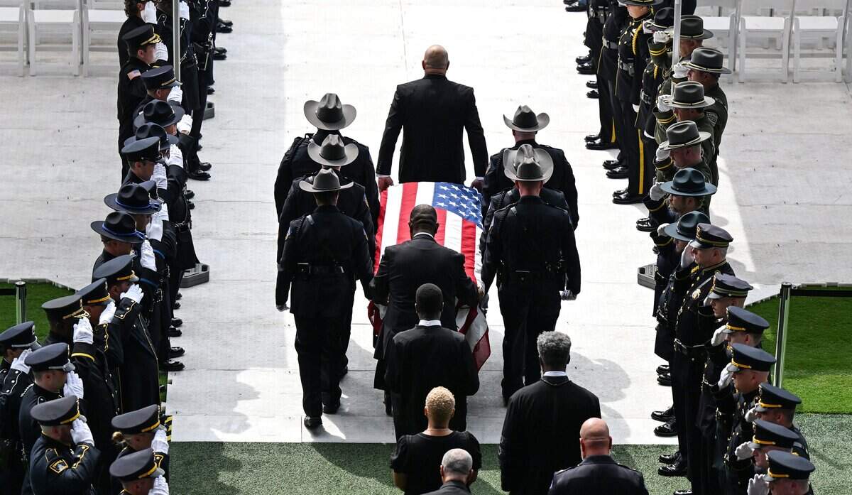 Law enforcement officers salute while pallbearers carry the casket of Wyandotte County Sheriff's deputy Elijah Ming through Children's Mercy Stadium on Monday, August 11, 2025, during funeral services for Ming. Ming was killed in the line of duty while responding to a call.