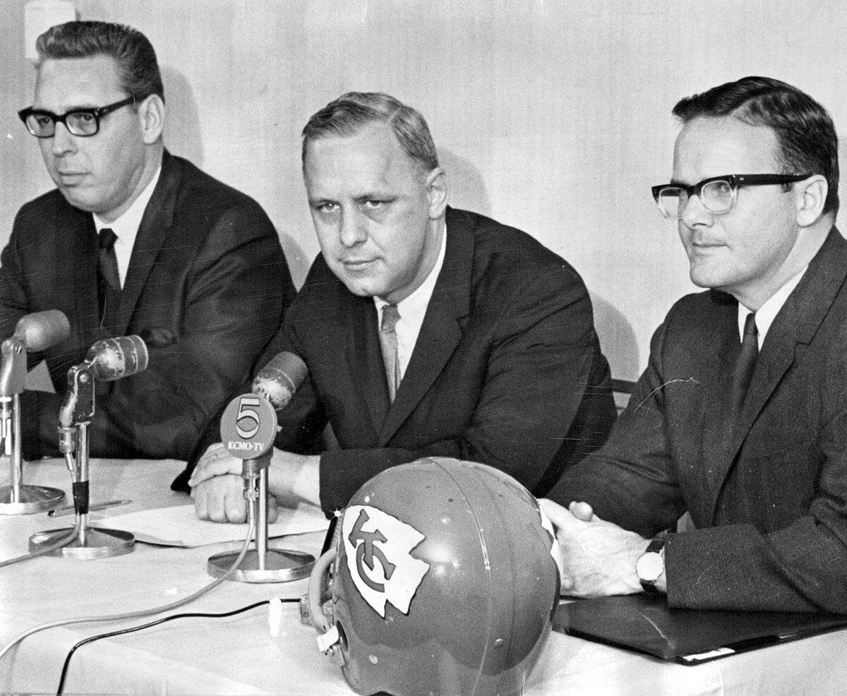 George Halas Jr., president and general manager of the Chicago Bears, is flanked by Kansas City Chiefs officials during a press conference announcing a preseason game in 1967. On his left is Jack Steadman, executive vice president and general manager of the Chiefs, and on his right is Lamar Hunt, owner of the Kansas City Chiefs.