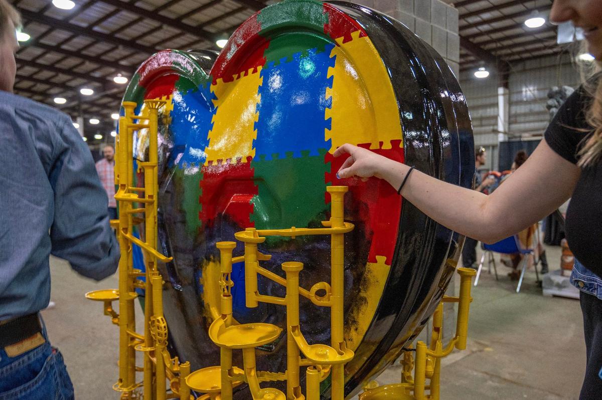 A visitor places a blue marble into a contraption featured in the heart display titled “The Blue Marble” by artist Meranda McDermott.