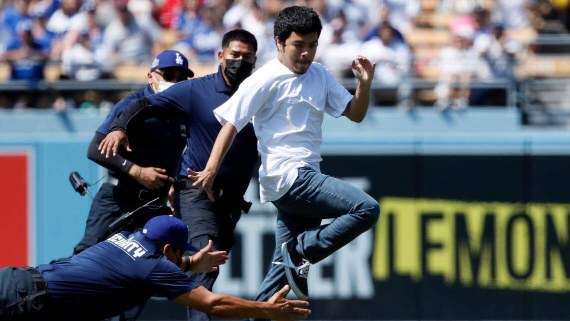Los Angeles Dodgers security guard dives to try to catch a spectator that ran on the field during the sixth inning of a baseball game against the Los Angeles Angels in Los Angeles, Sunday, Aug. 8, 2021. (AP Photo/Alex Gallardo)