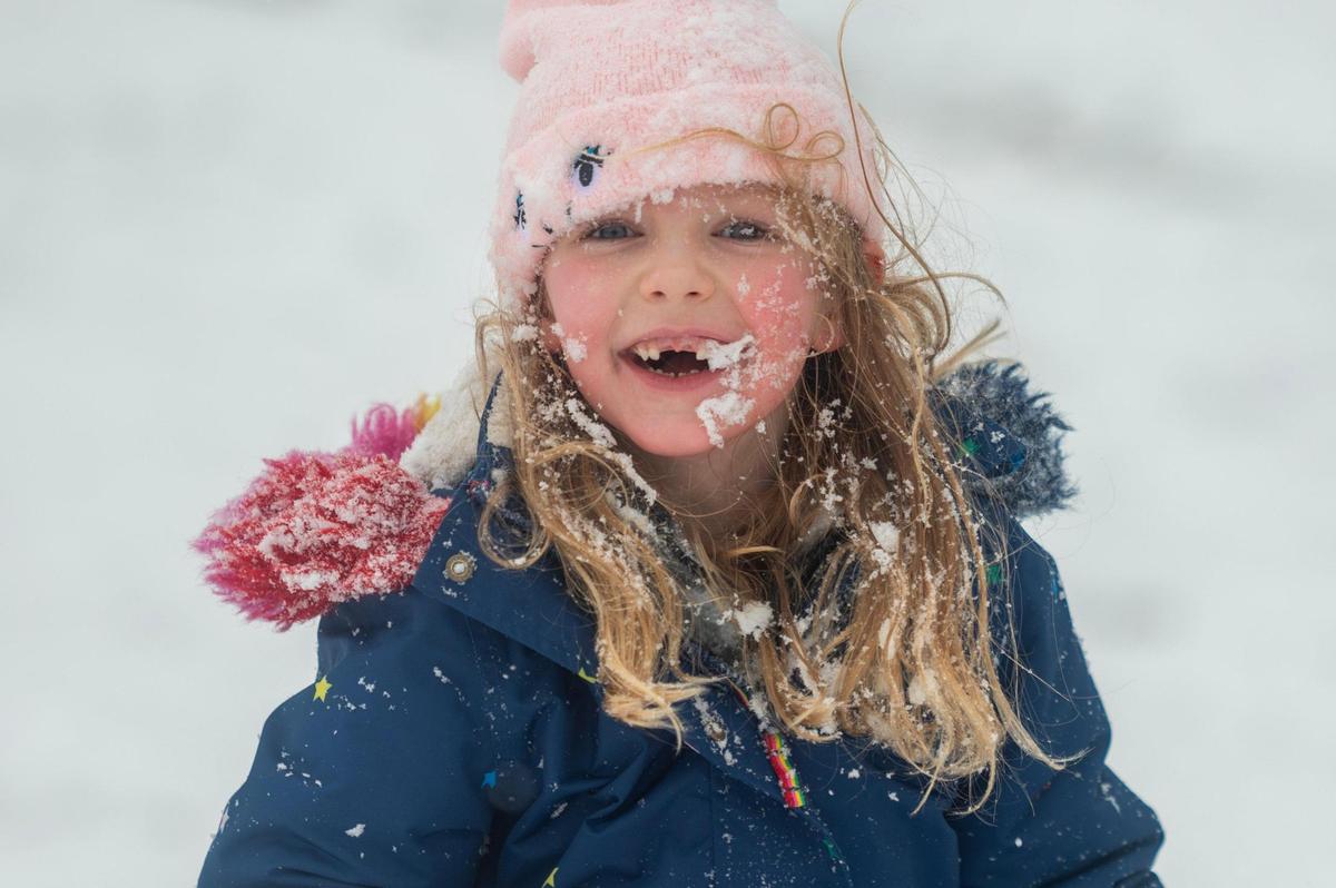 Five-year-old Ada Cardwell laughs with a snow-covered face after sliding down a hill at Hyde Park in Kansas City on Tuesday, Jan. 9, 2024.