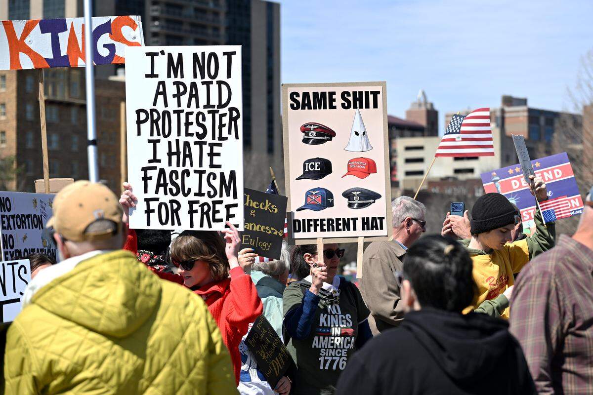 Protesters hold up signs during a No Kings protest at Mill Creek Park near the Country Club Plaza on Saturday, March 28, 2026, in Kansas City.