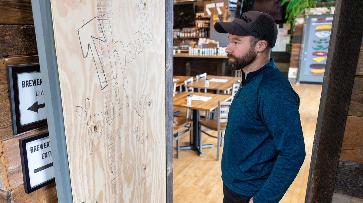 Brewer’s Kitchen and Corner owner Chris Riggins shows the boarded-up front door someone broke out during a burglary in late August.