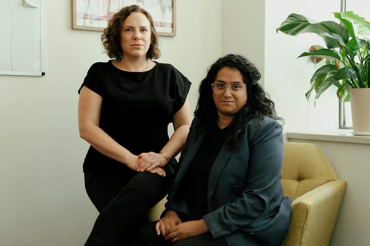 Two attorneys, a White woman and an Indian woman, pose for a portrait in their office.