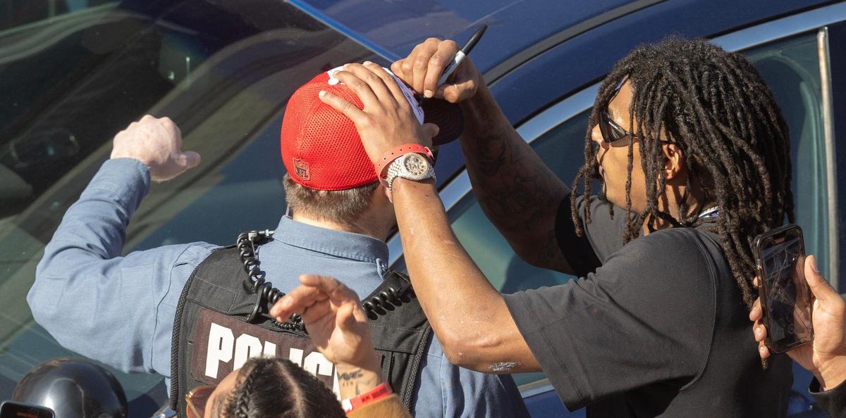 Isiah Pacheco stops to autograph the hat of a law enforcement officer as the Chiefs make their way down Grand Boulevard during the Super Bowl parade on Wednesday.