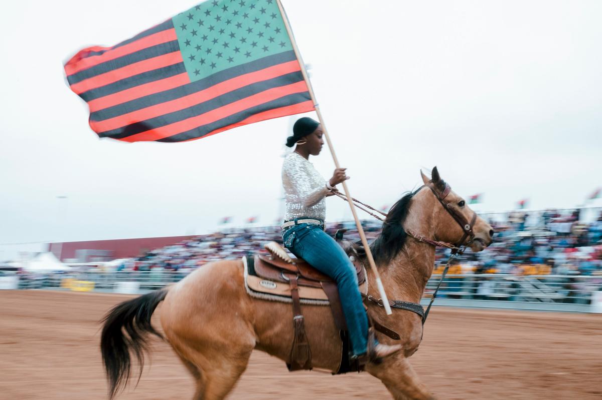 In this photo captured by Black rodeo photographer, Ivan McClellan, a horsewoman carries the Black pride flag while the Black national anthem played a rodeo event among many that McClellan has photographed.