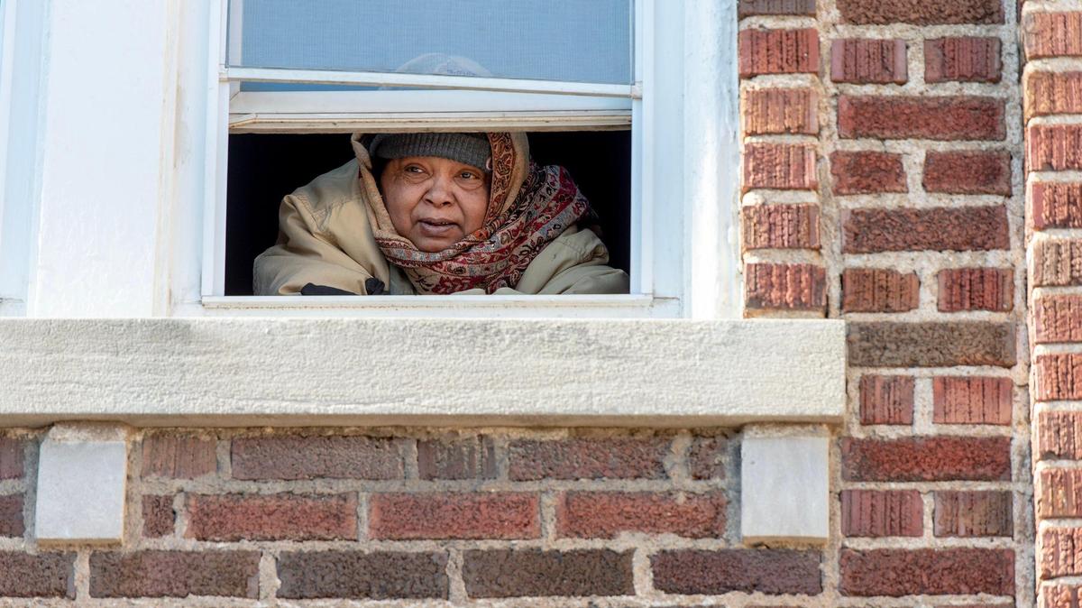 A woman, bundled up in winter clothing, looks out from her apartment on Monday, Jan. 23, 2023, in Kansas City. The multi-family housing unit has been without heat since early Friday morning.