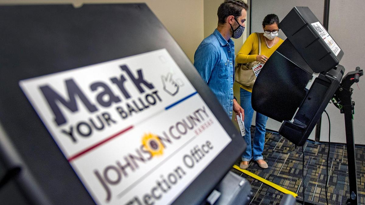 In this August 2020 file photo, election worker Andrew Presnal (left) assists voter Tia Mirocke at the voting machine as she voted in the Johnson County election in Mission, Kansas.