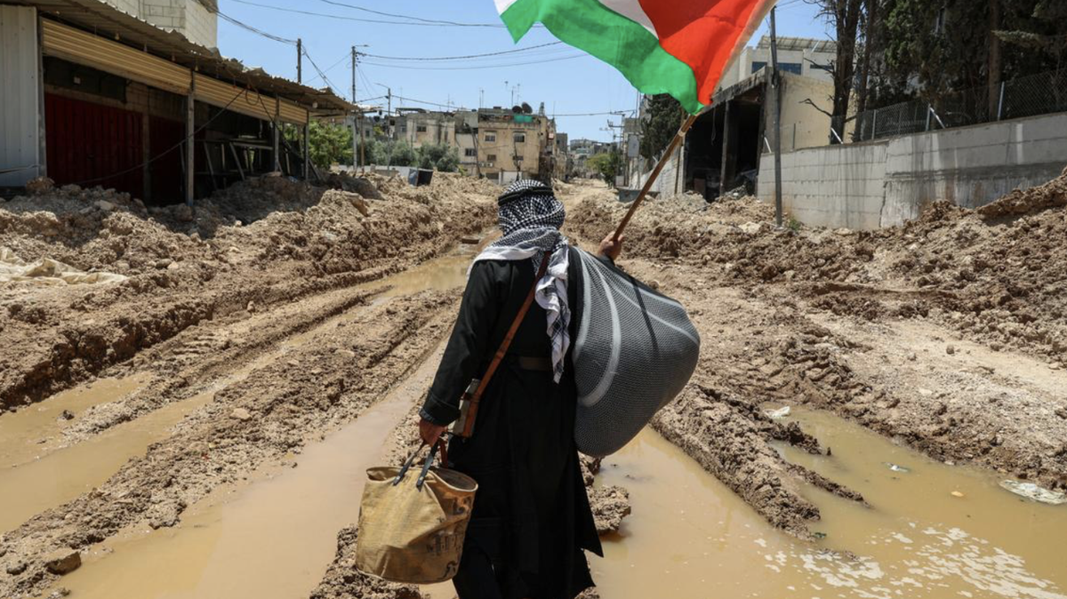 Palestinian Man in West Bank. A Palestinian man lifts a national flag as he walks on a road destroyed in Israeli raids in occupied West Bank, where Missouri resident Robert Suberi remains after his release from Israeli forces.