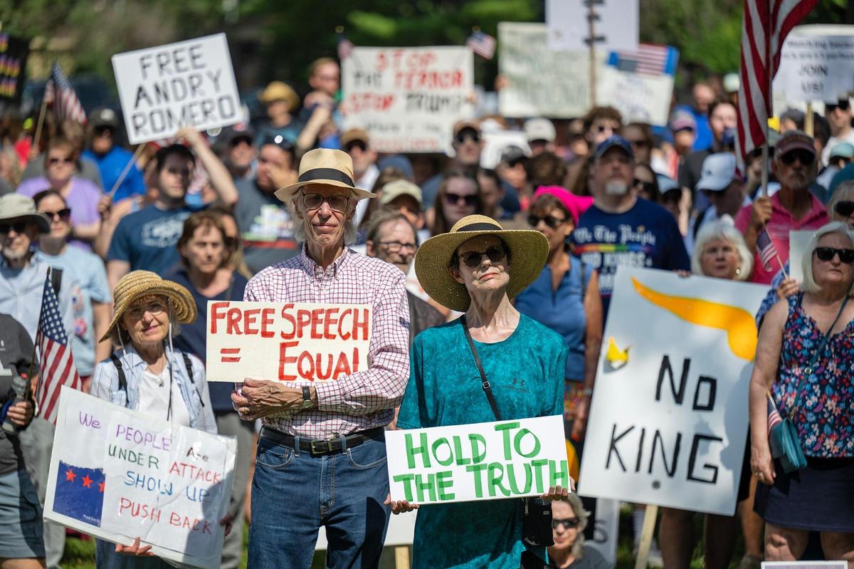 Protesters Roderick and Wyatt Townley, center, of Johnson County, stood among a large crowd and listened to spearkers as part of a nationwide “No Kings” day of defiance on Saturday, June 14, 2025, at Sar-Ko-Par Trails Park in Lenexa, Kansas. The events protest President Donald Trump and immigration policies, among other issues.