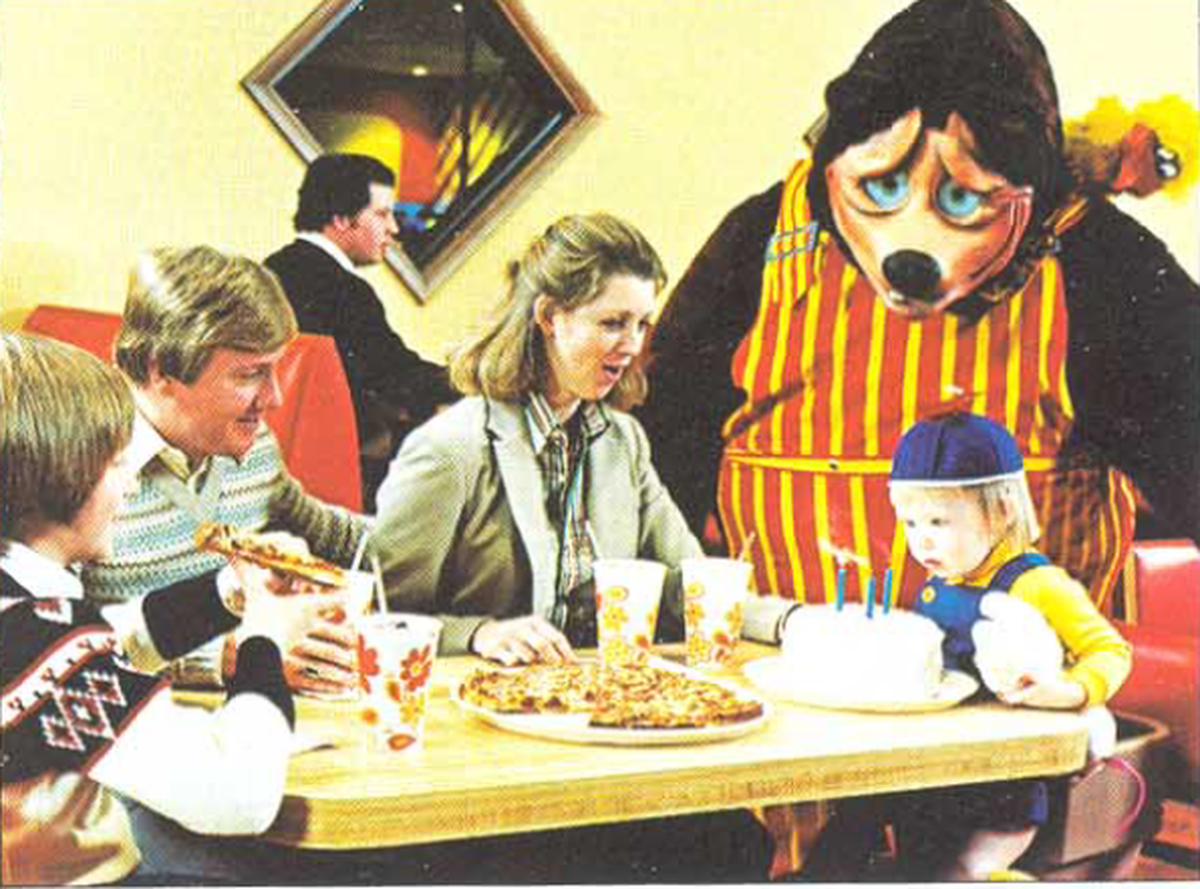 Billy Bob Brockali greeted a family at the first ShowBiz Pizza restaurant, located in Kansas City at the Antioch Center. The image comes from a 1980 flyer for prospective franchisees that is archived on ShowBizPizza.com.
