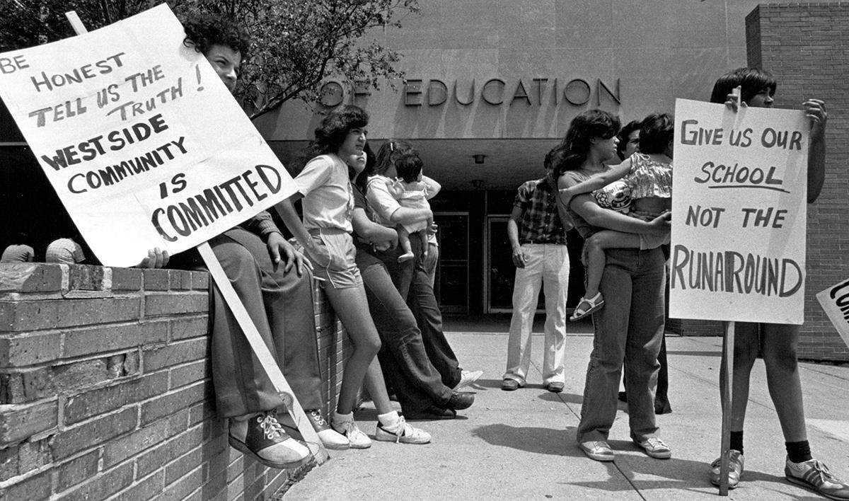 West Side residents continue their peaceful protest at the Board of Education administration building, seeking an answer on the fate of a proposed experimental school for their community. School board members say that their commitment to the school stands but that the budget is uncertain.