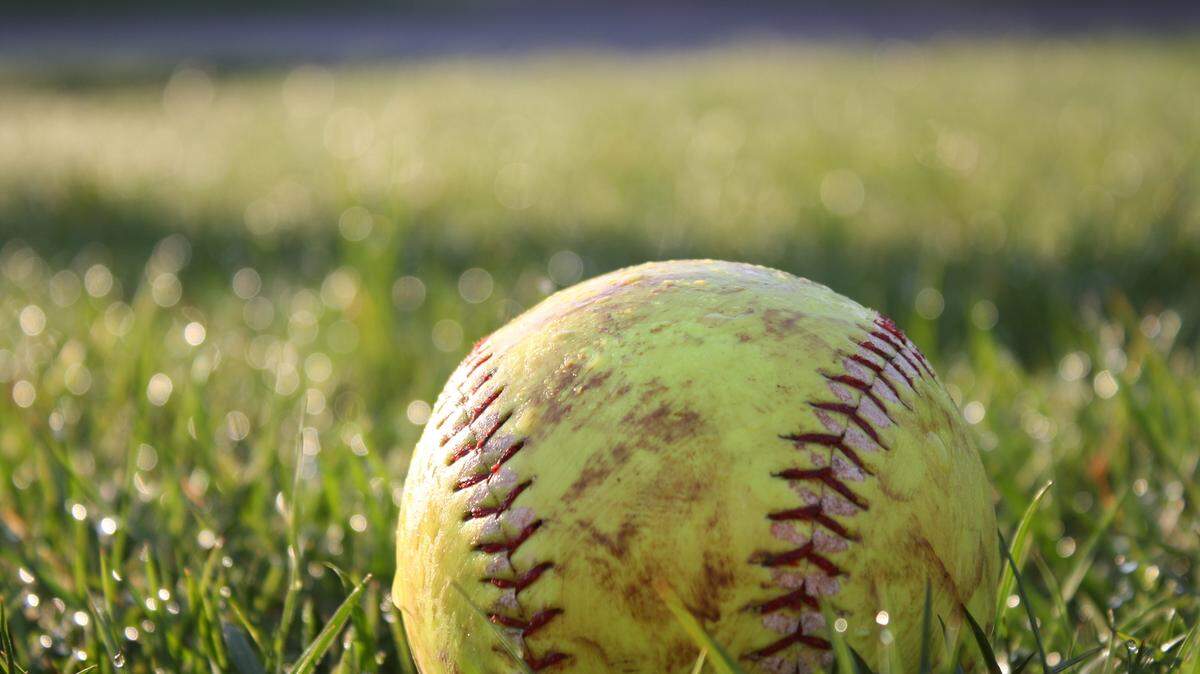A softball in the grass while the sun rises.