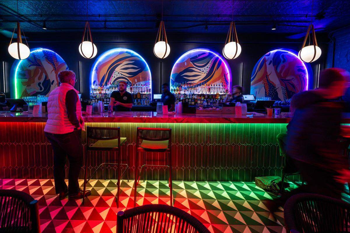 Rainbow lights, murals, and a large display of liquor bottles are seen in the main bar area at Q Kansas City in Westport.