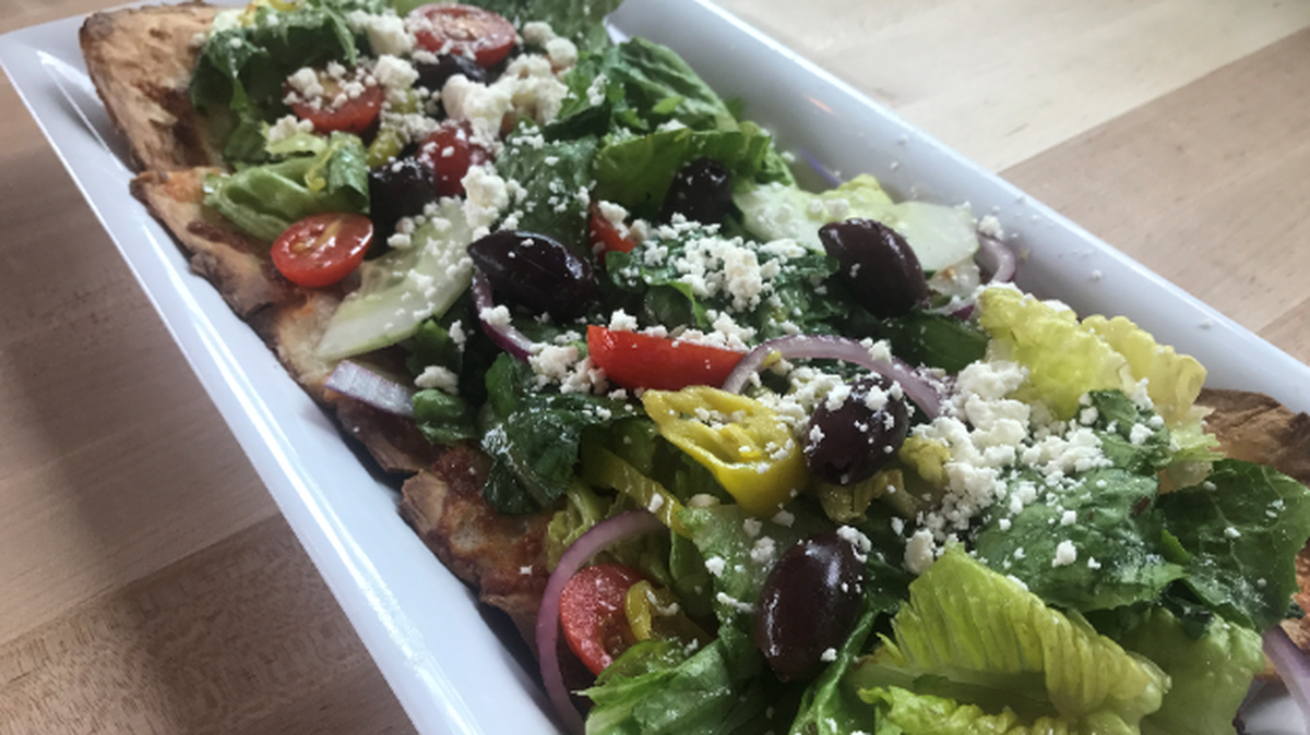 Flying Horse Taproom’s Greek Goddess Pizza: a crispy flatbread crust topped with its Greek salad, melted mozzarella and an olive oil drizzle.
