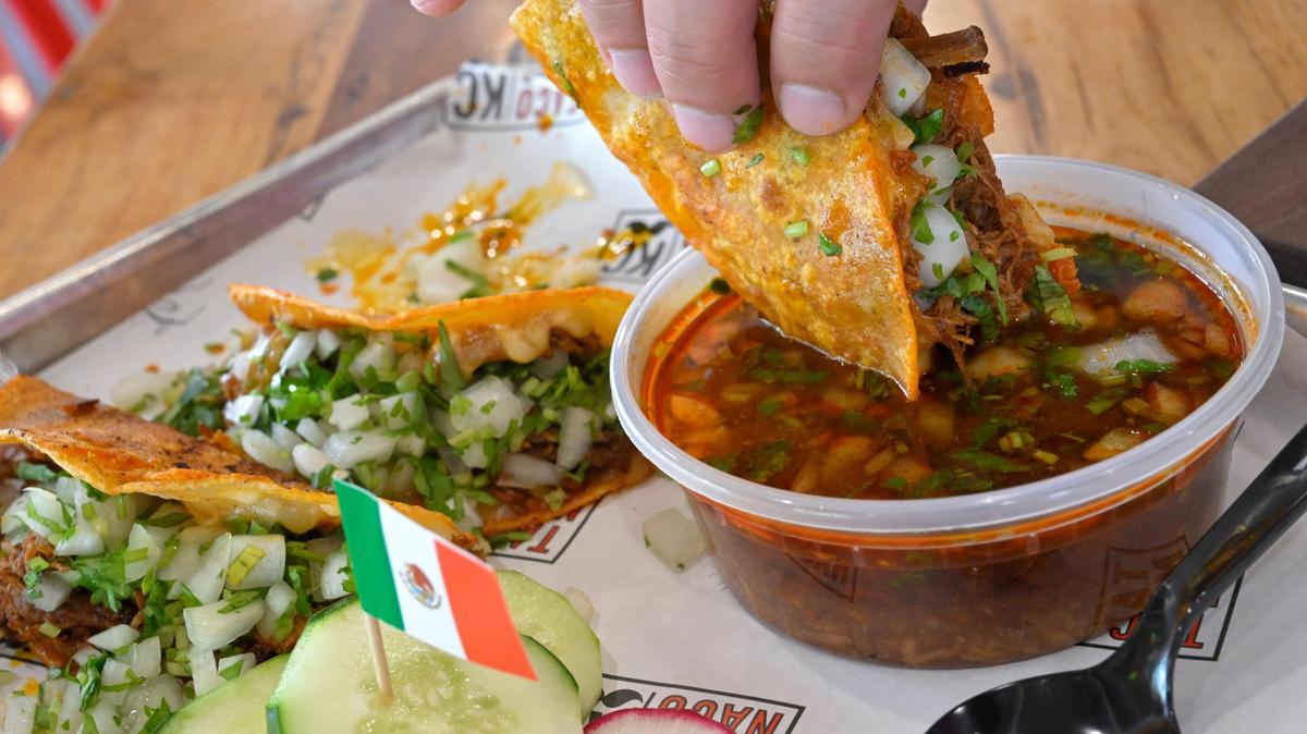 A quesabirria taco with white onions and cilantro is dipped in an au jus consummé at Taco Naco.