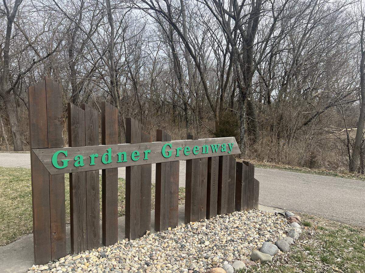 The Gardner Greenway sign is pictured in front of a trail and wooded area.