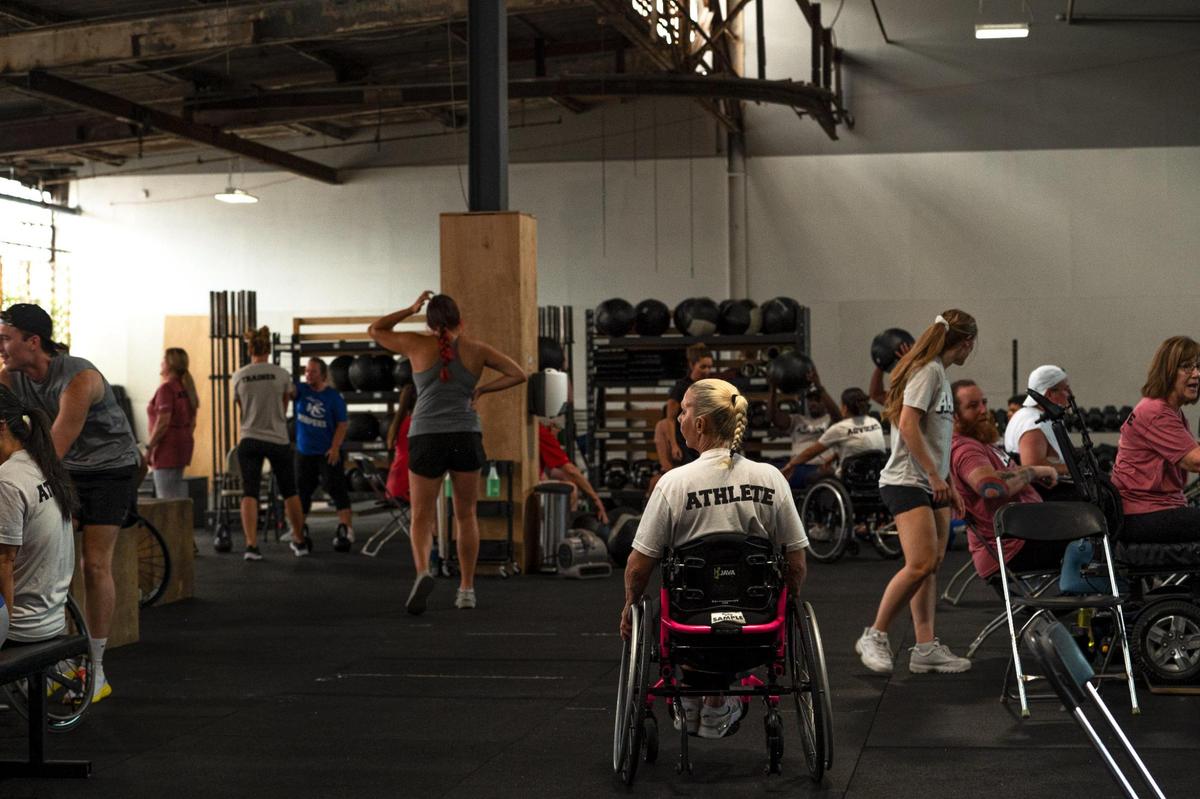 Lainie Rodgers wheels herself through a crowd of athletes during an Adaptive Athletes in Motion fundraising event on at Brave Enough CrossFit in Kansas City.