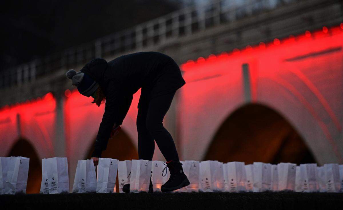 Jill Henning lights some of the 300 candle luminaries—each representing a Cambria County resident who died from COVID-19 are shown on a river wall near the historic Stone Bridge in Johnstown, Pa., Tuesday, Jan. 19, 2021.