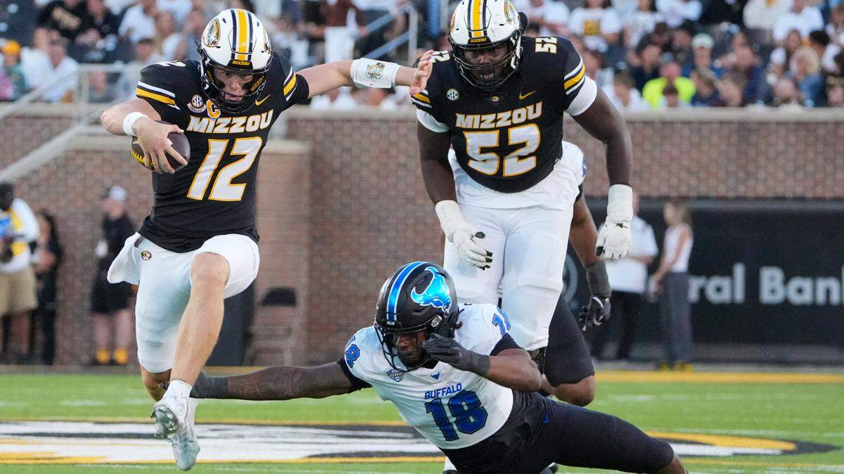 Missouri quarterback Brady Cook, left, leaps Buffalo Bulls linebacker Dion Crawford en route to one of his Saturday evening touchdowns for the Tigers at Faurot Field at Memorial Stadium.