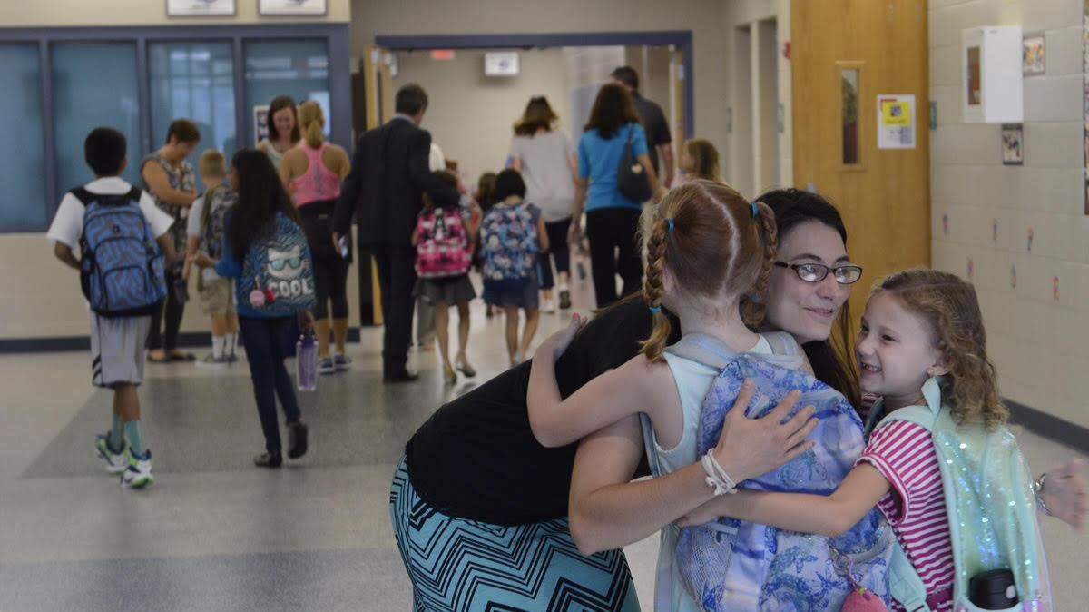 Art teacher Laura Reece hugs Calley Portsche (left) and Eliot Zolton (right) as they arrive on the first day of school at Cedar Creek Elementary School on Wednesday. 