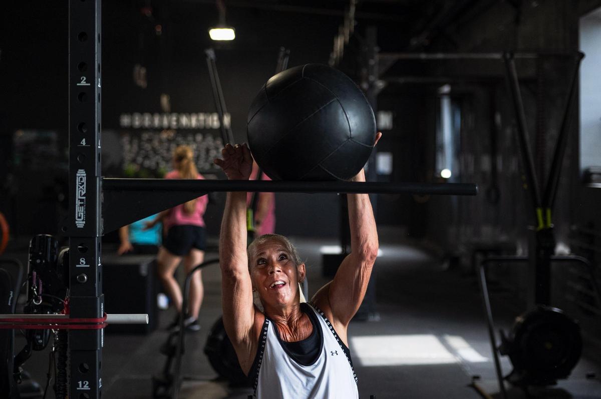 Lainie Rodgers lifts a medicine ball over a pull up bar at Brave Enough CrossFit in Kansas City. She says the Adaptive Athletes in Motion program has transformed her mobility and her confidence.