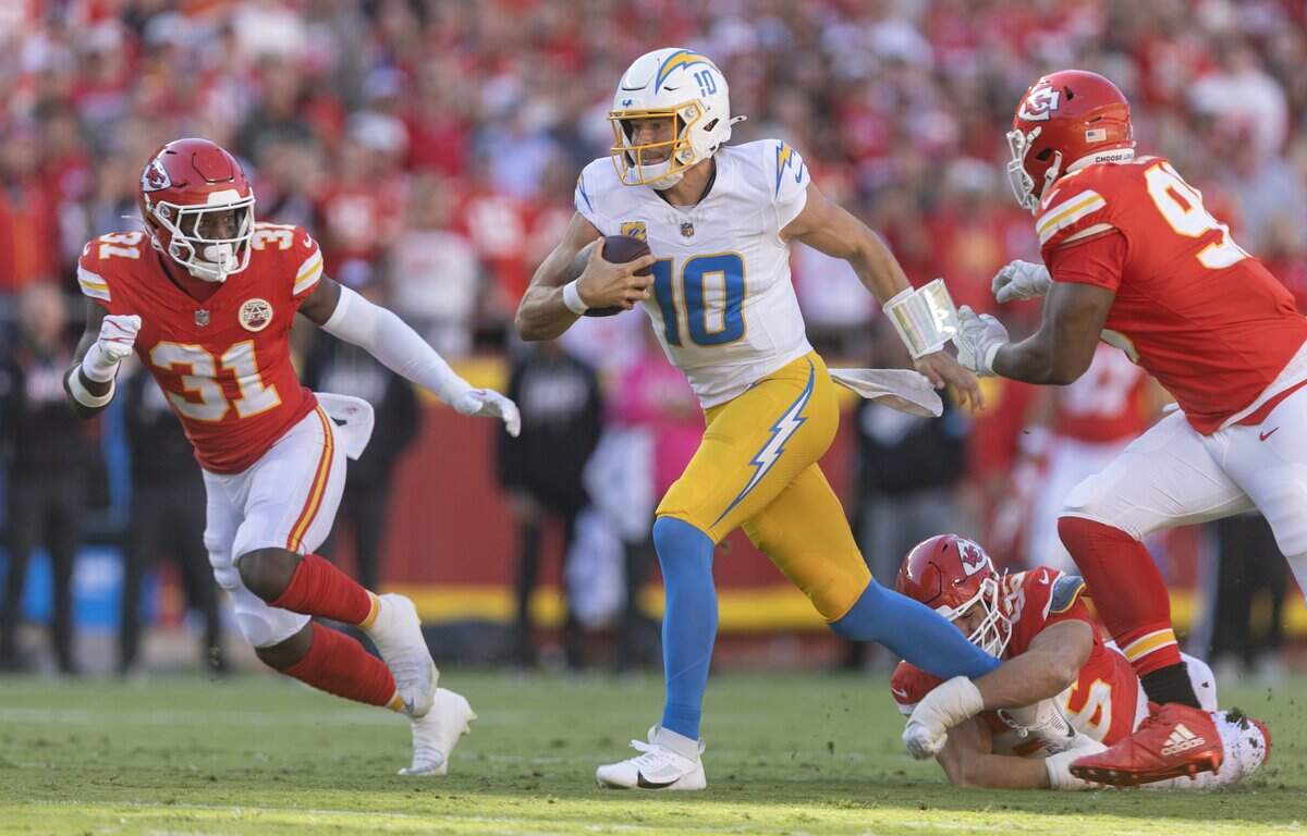 Los Angeles Chargers quarterback Justin Herbert (10) escapes the tackle of Kansas City Chiefs defensive end George Karlaftis (56) during the first half on Sunday at Arrowhead Stadium.