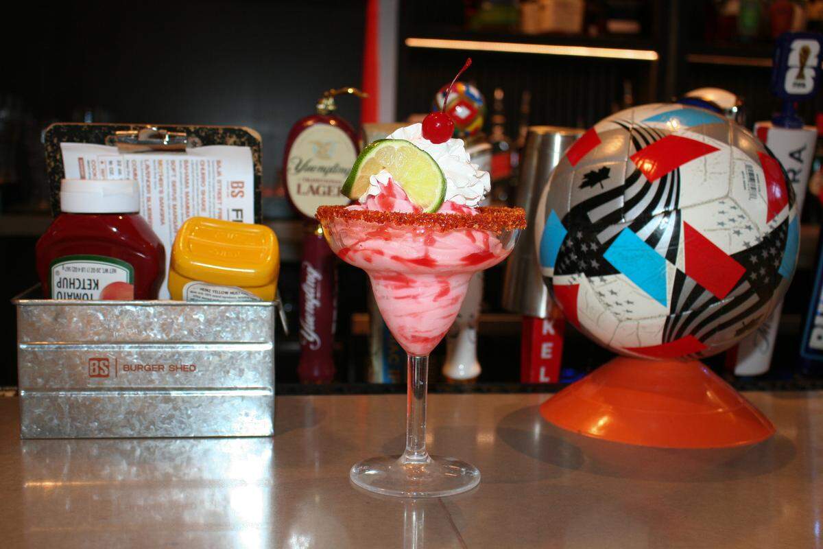 The strawberry soft-serve margarita served at Burger Shed is topped with whipped cream, a cherry and a lime.