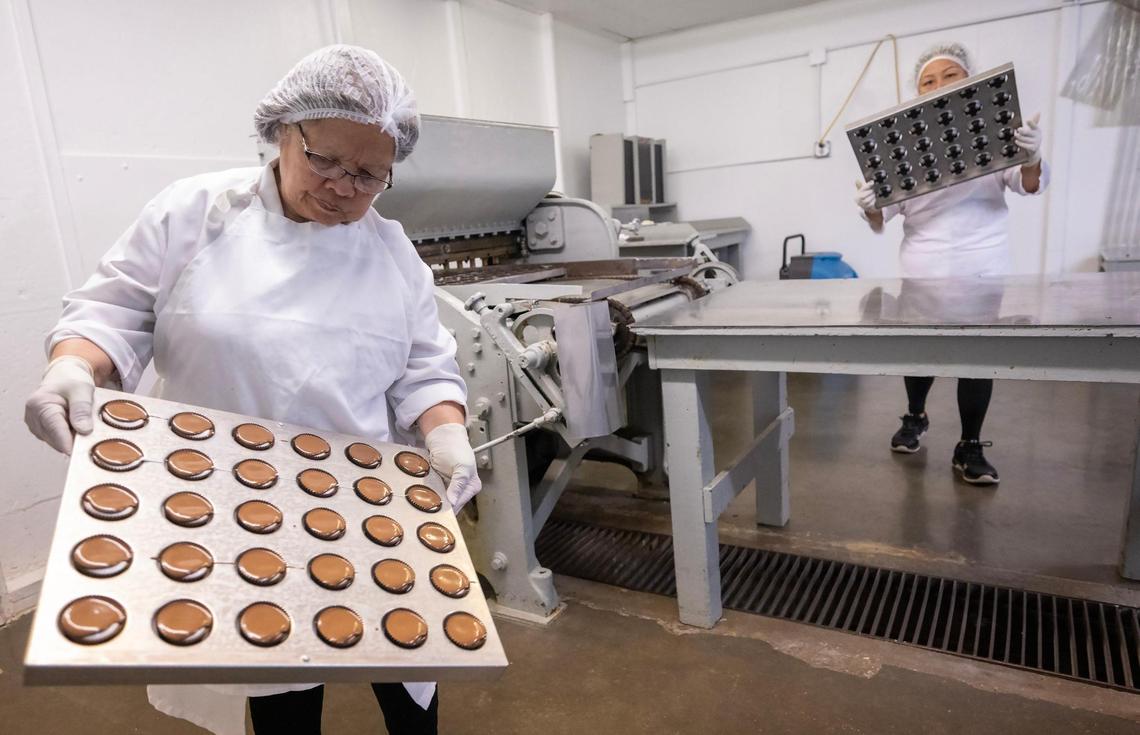 Viet Swiercinsky, left, and Keo Vongchantha check freshly produced trays of Valomilks, tilting them to make sure the warm chocolate evenly coats the marshmallow-filled cups.