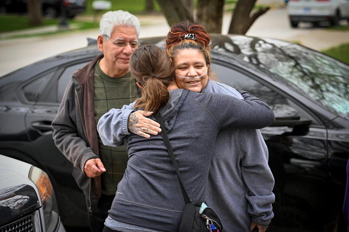 After being hospitalized since January with COVID-19, Kansas City police officer Lisa Sidenstick, right, is greeted and hugged by her cousin, Melanie Ruiz, as she arrived Wednesday at her Northland home. Sidenstick’s father, Joe Arce, left, founder and publisher of the bilingual newspaper KC Hispanic News, looked on.