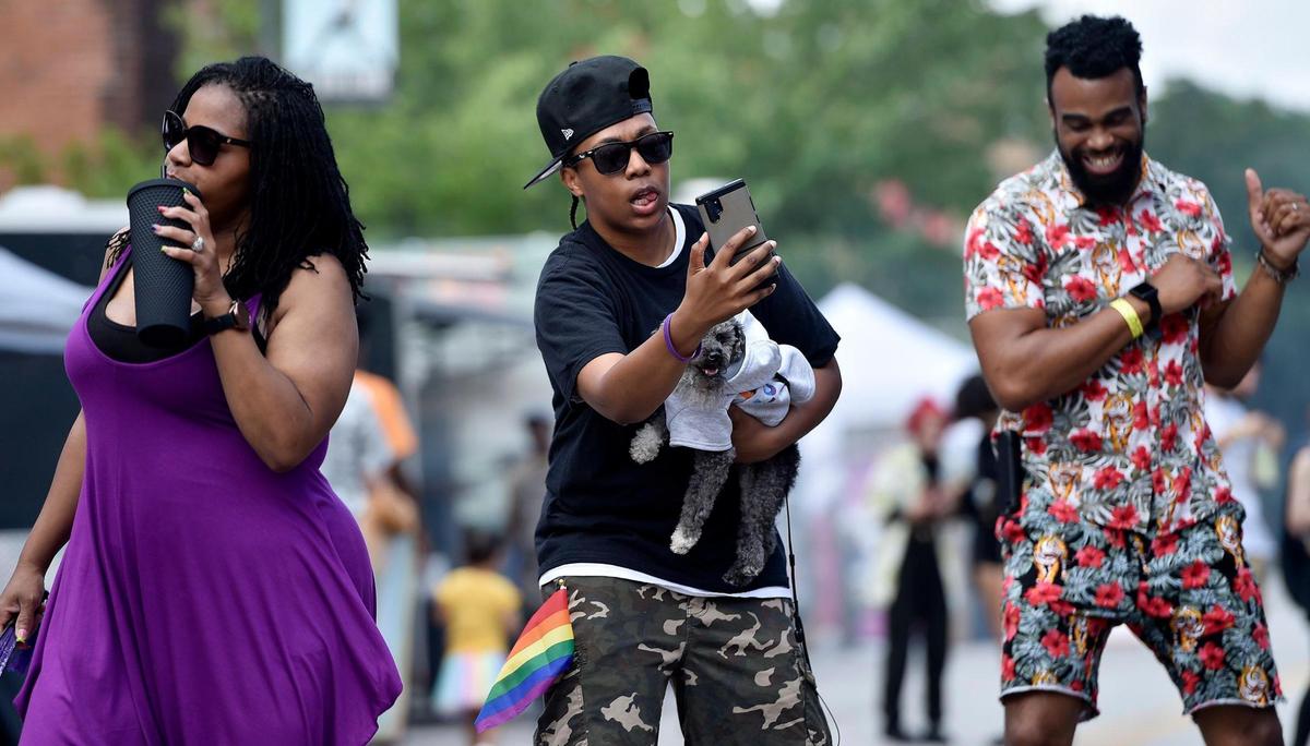 Lanesha Huggins of Kansas City, Kansas, center, records the moment while dancing with Jackson, a toy poodle, during the first Pride on the Vine 2021 at the 18th and Vine Jazz District Saturday, June 26, 2021. Dancing alongside of Huggins are wife Tiffany Huggins, left, and Aaron Alexander of Kansas City.