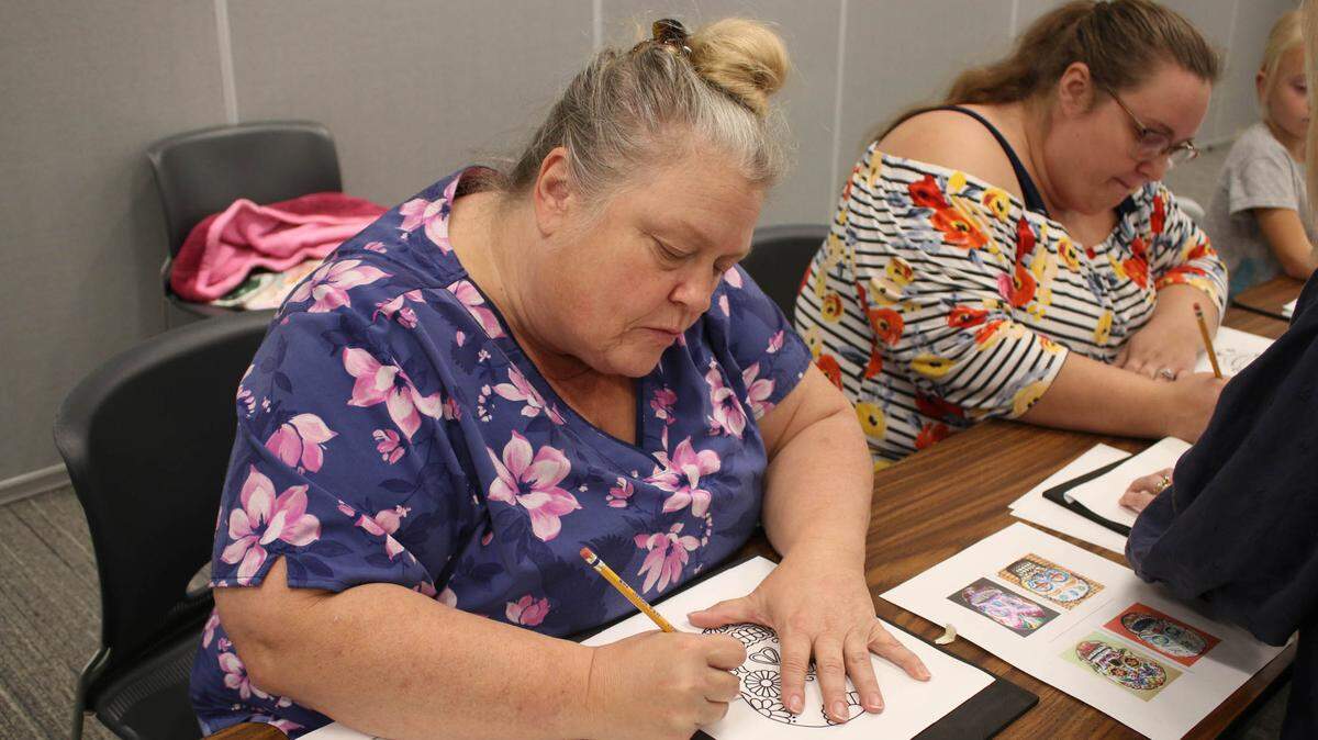 Bates City residents Rachel Reese and Amanda Offill trace sugar skull designs onto their sheets of tin during a workshop at the Lee’s Summit Library.