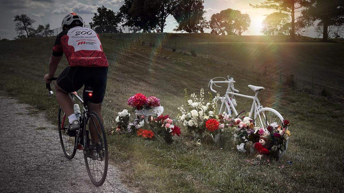 In this photo, provided by Jeremy “JC” Van Deventer, he bicycles past a memorial for Charles Criniere, who was killed Aug. 27, 2022, in a hit-and-run crash on View High Drive near the intersection of Longview Road. Van Deventer is helping organize a memorial ride for Criniere, scheduled for Sept. 17. All proceeds will go to help Criniere’s wife and 10 children.