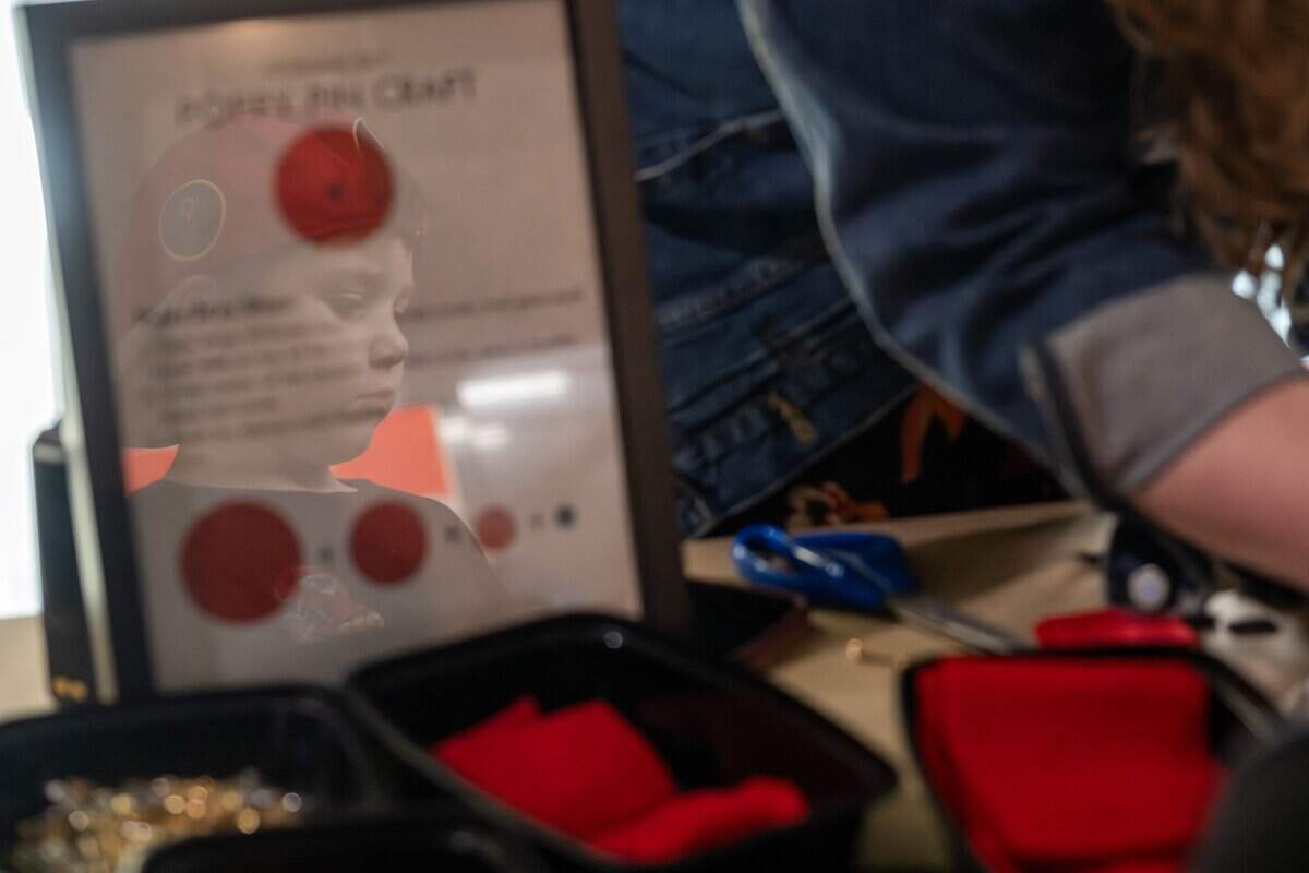 The reflection of 6-year-old Ethan Knudtson is seen on a bulletin board as he watches Madeline Thomas, education programs associate, explains how to make a felt poppy pin by the craft booth in honor of Veterans Day at the National WWI Museum and Memorial on Tuesday, Nov. 11, 2025.