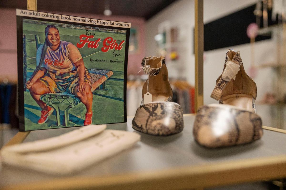 Alesha Bowman published an adult coloring book promoting body positivity for plus-size women. She displays it on a golden shelf in her shop.