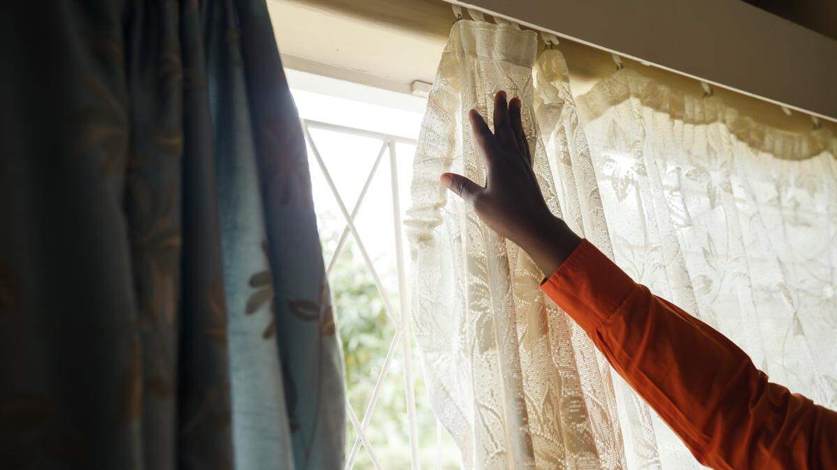A woman closes curtains. (Photo by Jekesai NJIKIZANA / AFP) (Photo credit should read JEKESAI NJIKIZANA/AFP via Getty Images)