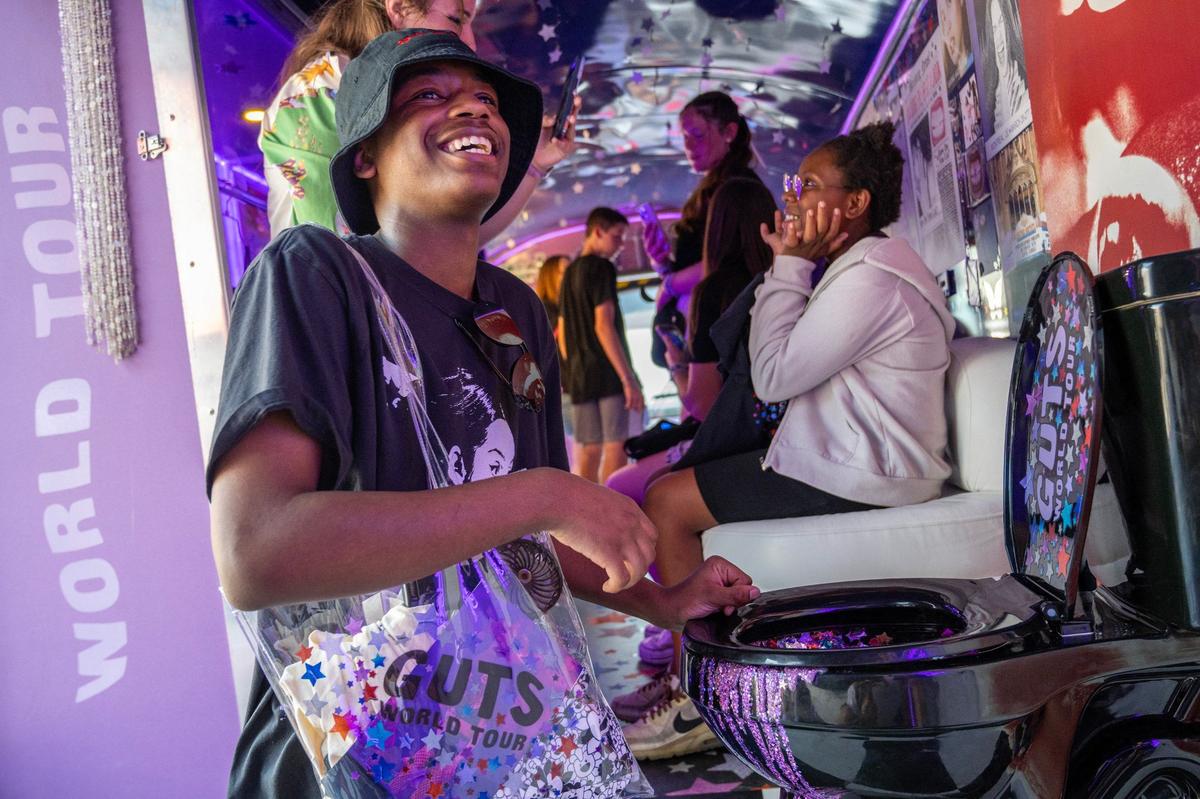 Elijah Russell laughs as he takes a photo next to a glitter-filled toilet while visiting an interactive exhibit aboard a themed bus before the Olivia Rodrigo Guts World Tour concert outside of T-Mobile Center on Friday, July 26, 2024, in Kansas City.