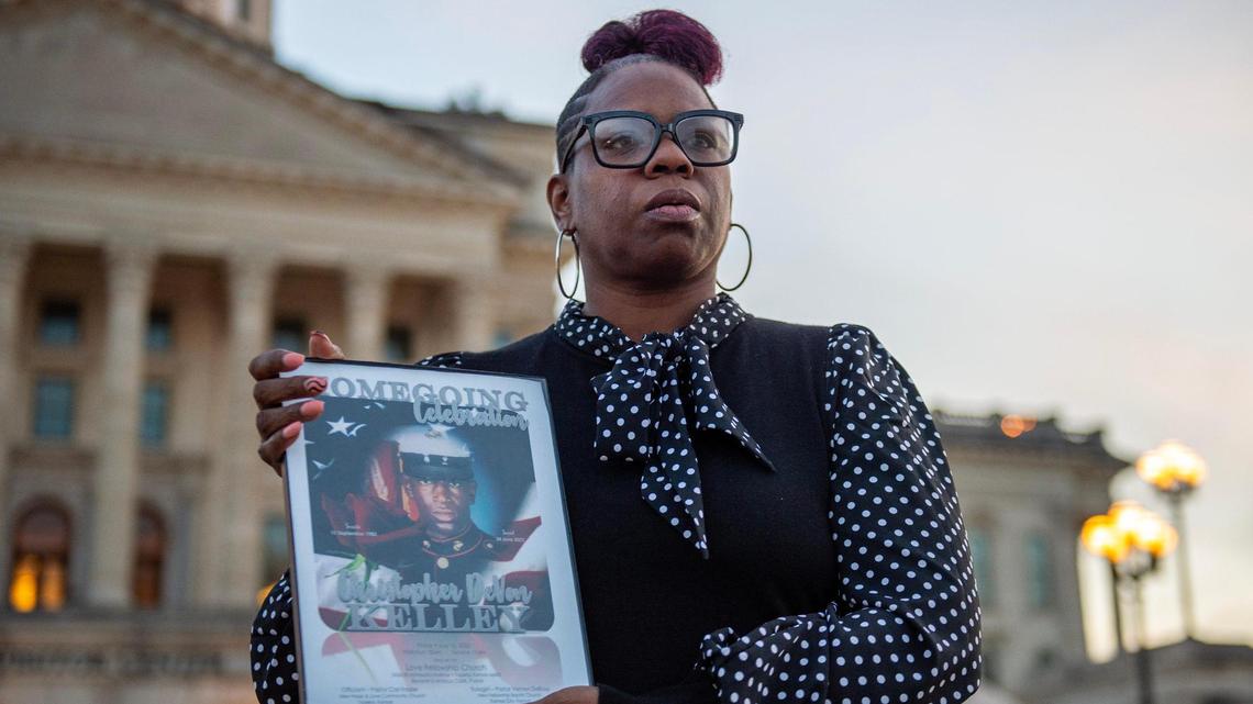 Christian Kelley showcases a framed photo of her brother Christopher DeVon Kelley in front of the Kansas Statehouse in Topeka. Officers shot and killed the Marine Corps veteran in June 2022.