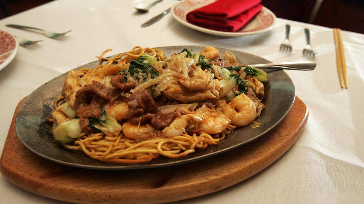 Princess Garden's Sizzling Double Face Yellow Noodles comes to the table in two parts: crispy noodles in one pan, the savory meat and vegetables, including baby bok choy, in a brown sauce on another. The waiter pours the meat and vegetables on top of the noodles.