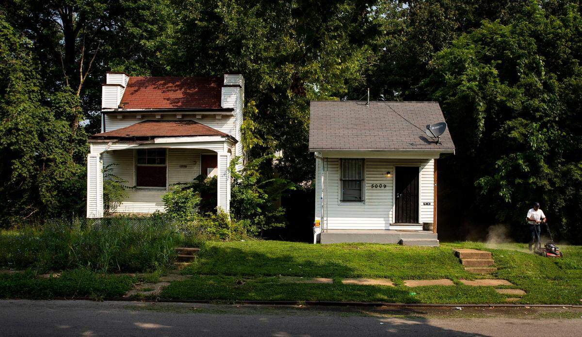 James Nick mows the lawn at his rental property (right) on Thrush Avenue in the Walnut Park East neighborhood of St. Louis, next to a vacant weed-infested property, on Friday, July 23, 2021. “What are people supposed to do that are trying to keep their properties clean?” Nick asks.