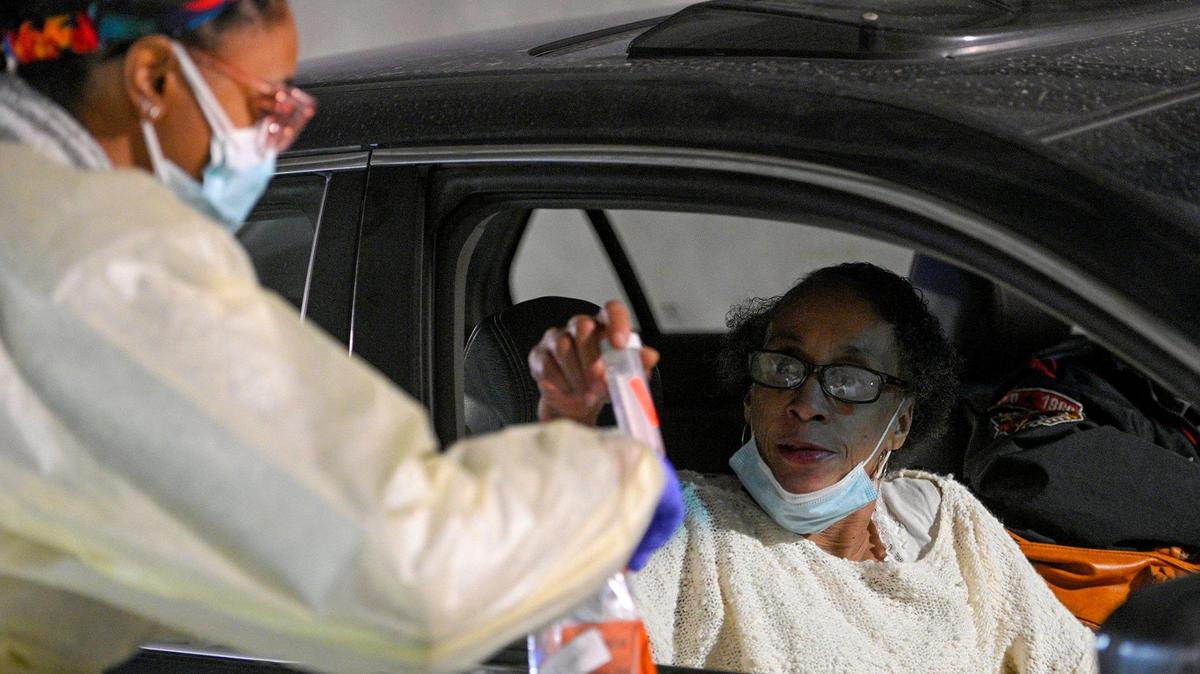 Theresa Harstad of Kansas City, right, hands her sample to registered nurse Brea Lewis at the University Health COVID drive-thru testing location on Friday.