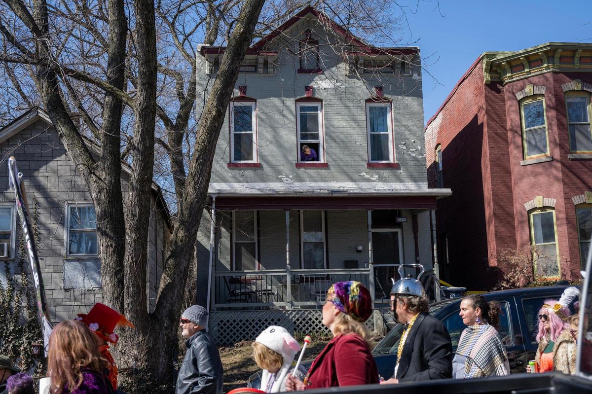 A neighbor looks out their window as the Krewe de Prank parade passes along Jefferson Street on Sunday, March 2, 2025, in Kansas City.