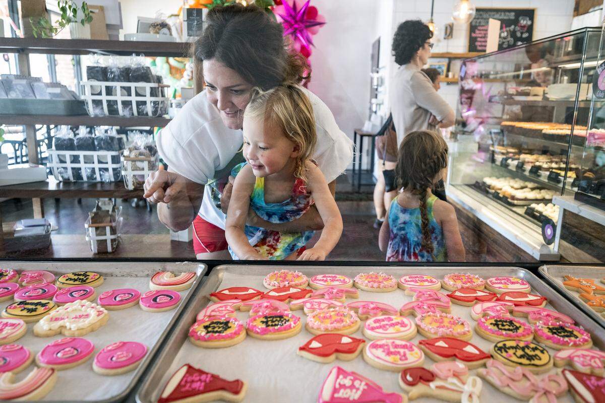 Brittany Tilander of Kansas City holds Celine Wirtz, 2, who selects some Chappell Roan-themed cookies on Thursday, October 2, 2025, at Dolce Bakery in Prairie Village. Local bakeries are seeing a significant demand for cookies to celebrate pop stars Taylor Swift and Chappell Roan.
