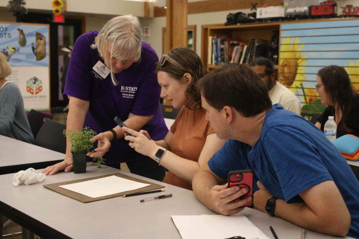 Johnson County Extension master gardener Mary Matthew shows a sample of marjoram to Kat Priest and Johnny Priest so they can take reference photos. Rain forced the class to do all their drawing inside the Overland Park Arboretum’s education center.