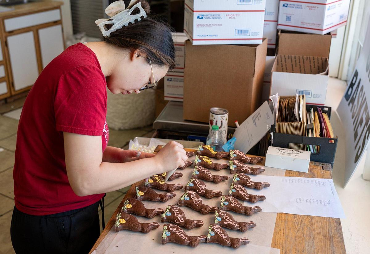 Laura Logan pipes names in white chocolate frosting onto handmade chocolate Easter bunnies at Laura Little’s Candies in Prairie Village.