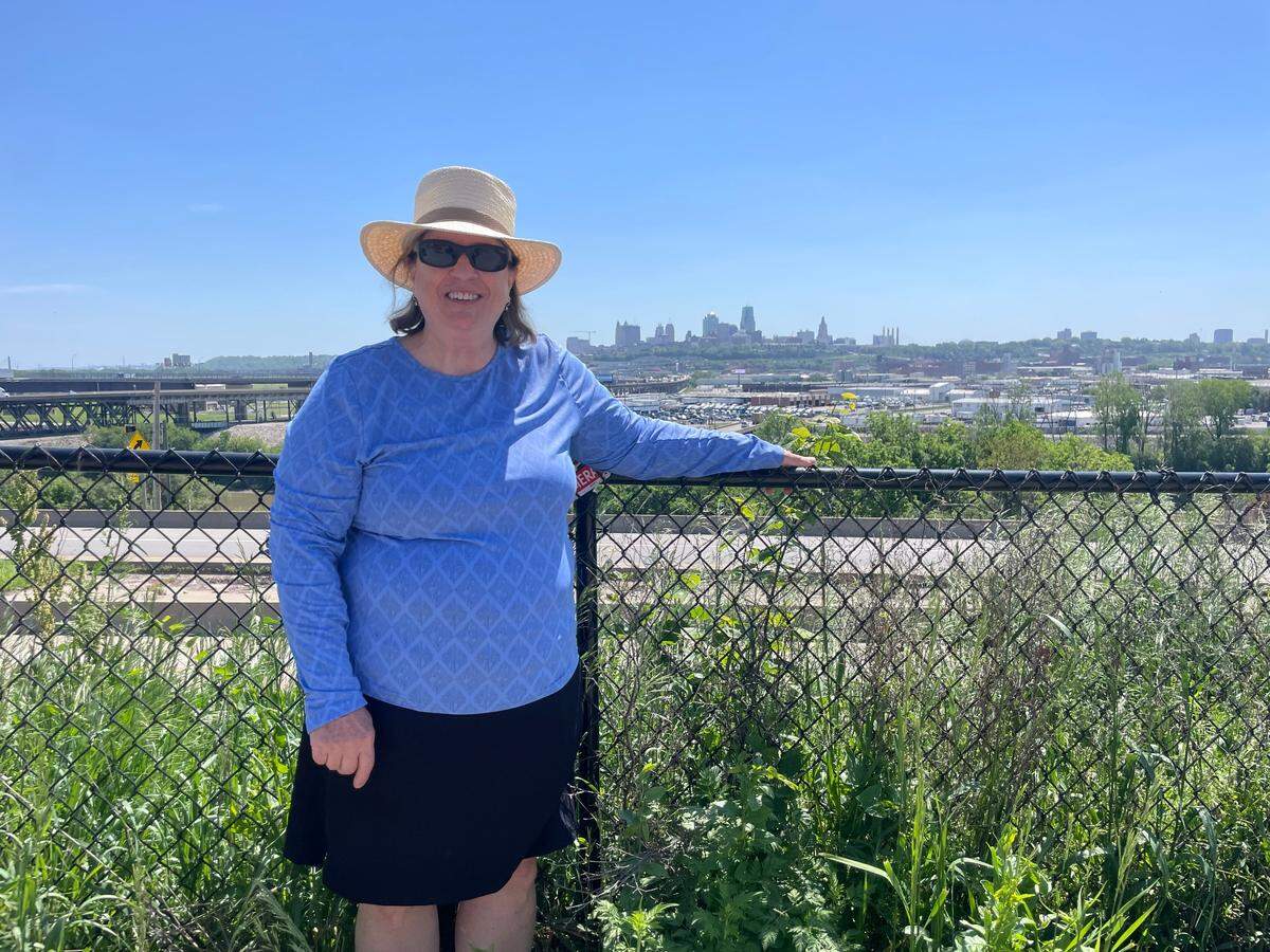 Rose Eilts, president of the Strawberry Hill Neighborhood Association, stands at the fence in front of her property with the Kansas City skyline in the background.